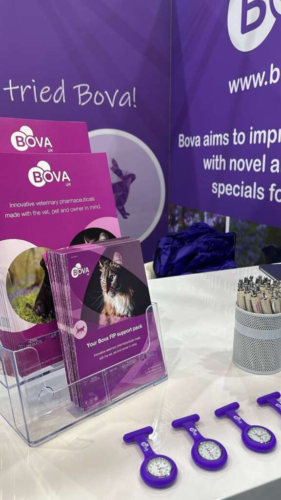 Bova UK booth featuring brochures on FIP support for cats, purple clip-on watches, branded pens, and signage promoting our innovative veterinary pharmaceuticals.